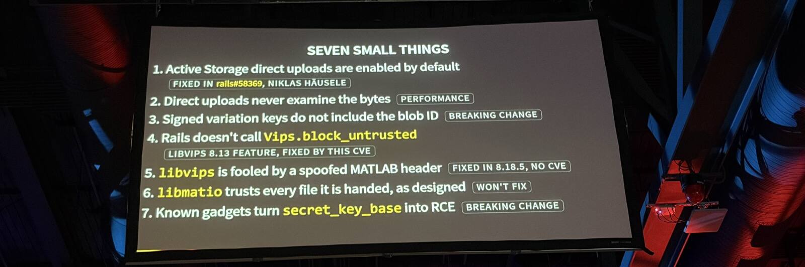 A slide titled 'Seven small things': 1. Active Storage direct uploads are enabled by default (fixed in rails#58369, Niklas Häusele). 2. Direct uploads never examine the bytes (performance). 3. Signed variation keys do not include the blob ID (breaking change). 4. Rails doesn't call Vips.block_untrusted (libvips 8.13 feature, fixed by this CVE). 5. libvips is fooled by a spoofed MATLAB header (fixed in 8.18.5, no CVE). 6. libmatio trusts every file it is handed, as designed (won't fix). 7. Known gadgets turn secret_key_base into RCE (breaking change)