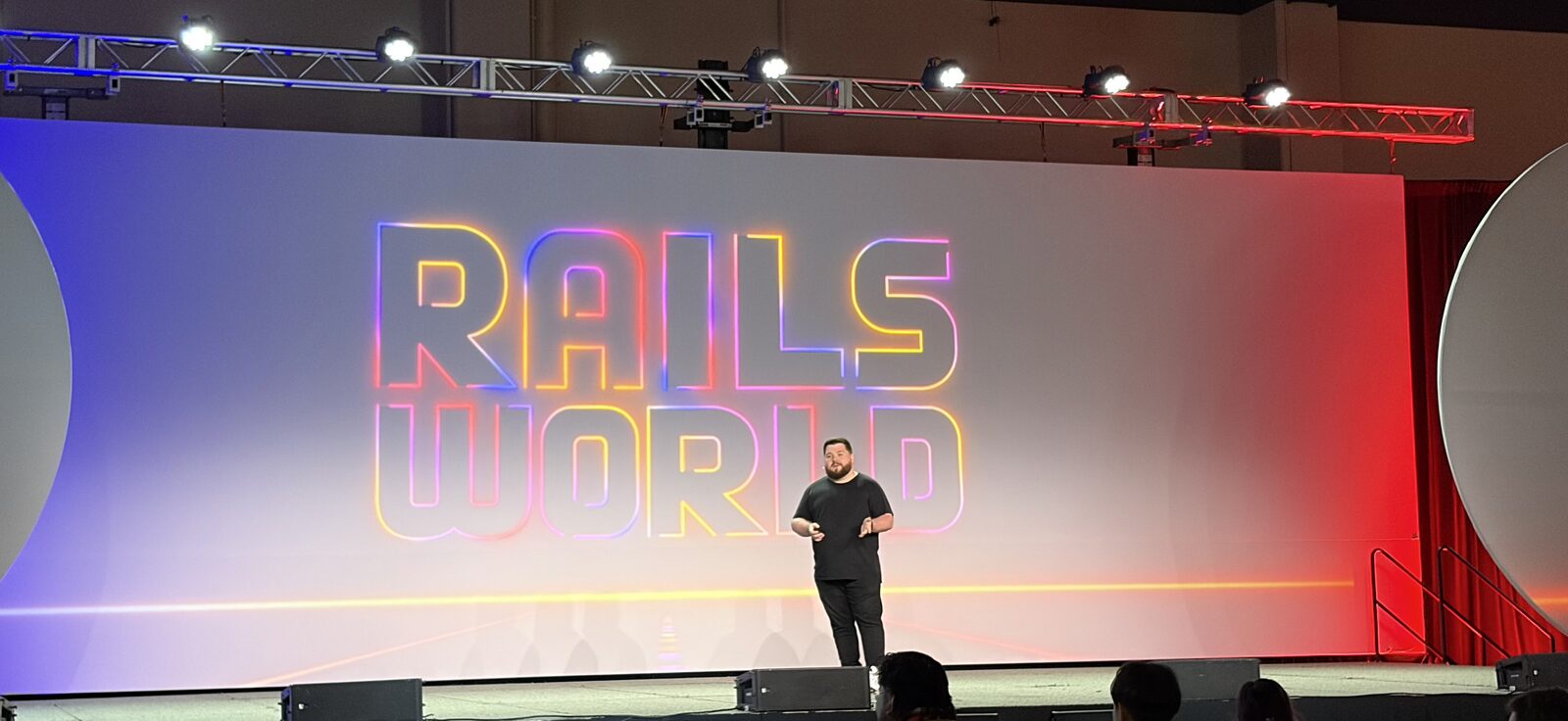 Marco Roth presenting on stage at Rails World 2026, in front of a large screen showing the glowing 'Rails World' logo