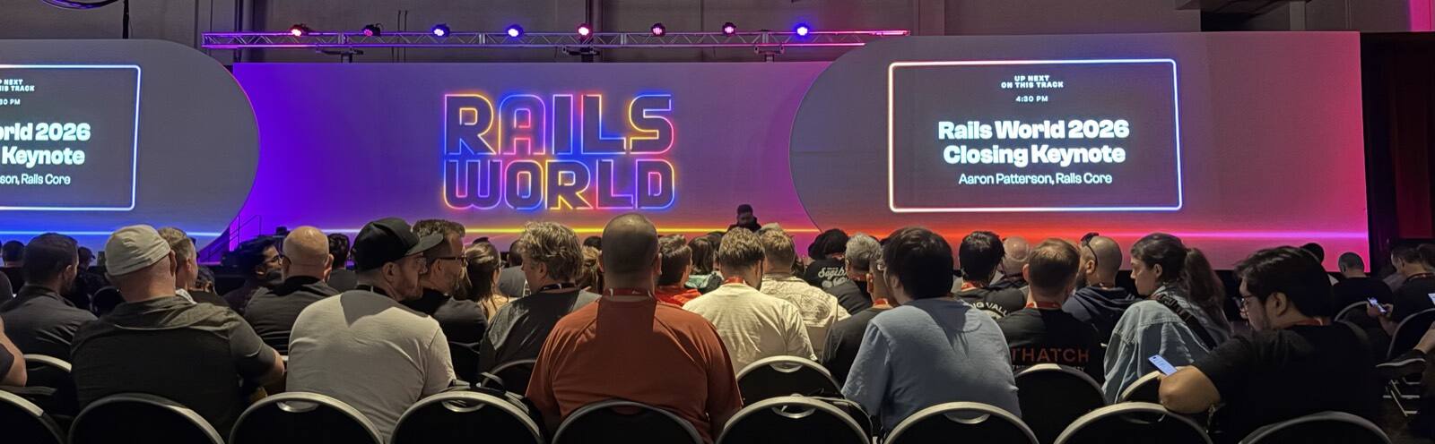 The Rails World 2026 main stage before the closing keynote, with screens reading 'Up next on this track: Rails World 2026 Closing Keynote, Aaron Patterson, Rails Core' above a packed audience