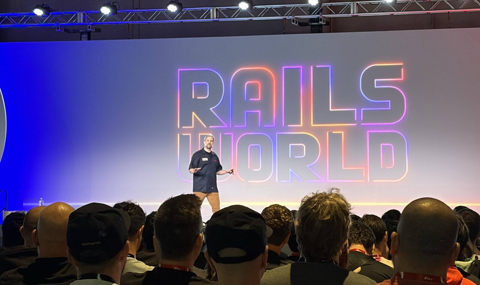 Aaron Patterson on stage at Rails World 2026, in front of the glowing 'Rails World' logo